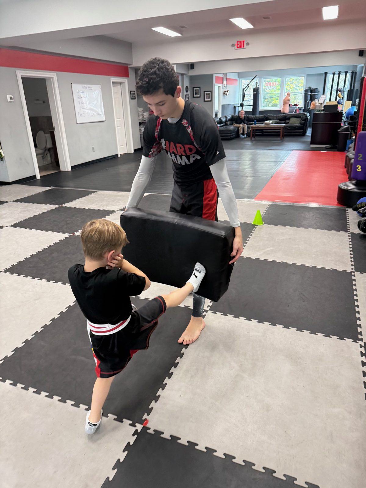 A young student kicking a pad held by a teen helper