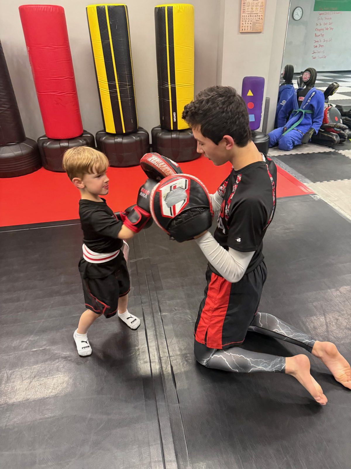 A teen helper holding focus mitts for a preschool student