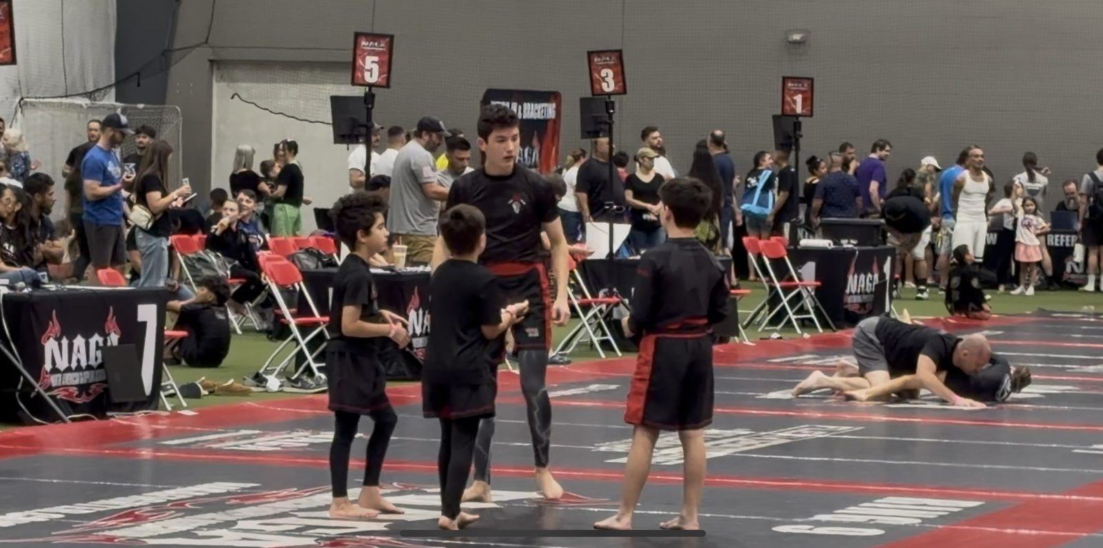 Ward MMA students in team shirts on the mats at a NAGA tournament