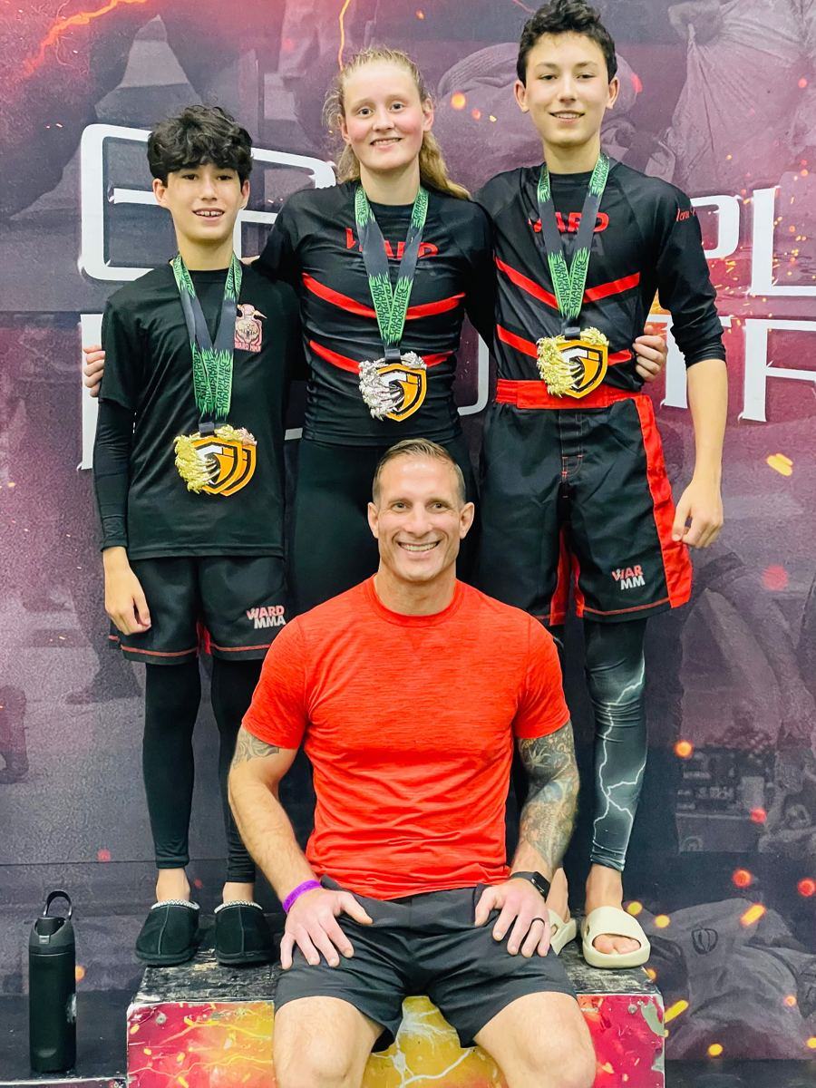 Three students on a tournament podium with gold medals and Coach Jay